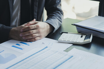 Close up of businessman clasped hands together on table with report documents. Concentrating before important negotiations, thinking or making decision, business concept.