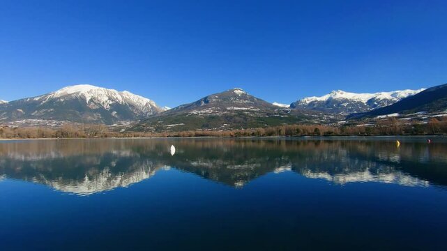 snowy mountain reflected on the lake of Embrun partially recovered of a thin layer of ice. Snowy mountains on the sides of a green one. Lot of copy space.