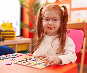 Fototapeta premium Adorable redhead girl playing with maths puzzle game sitting on table at kindergarten