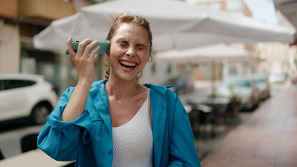 Young woman smiling confident listening audio message by the smartphone at street