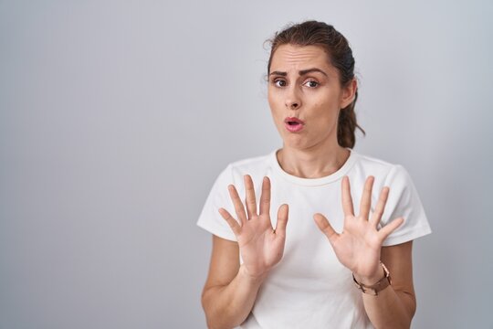 Beautiful brunette woman standing over isolated background moving away hands palms showing refusal and denial with afraid and disgusting expression. stop and forbidden.