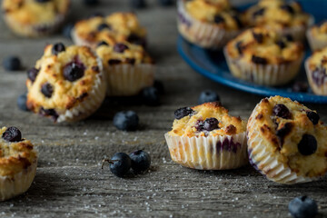 Several fresh homemade blueberry muffins scattered about on a rustic wood table.