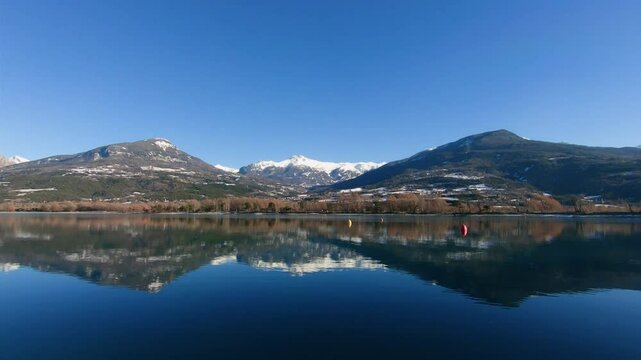 Embrun lake partially recovered thin layer ice reflecting mountains winter. Snowy mountain in center of two others