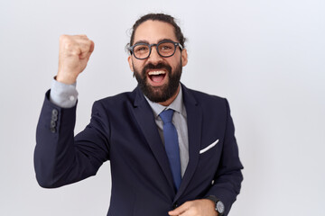 Hispanic man with beard wearing suit and tie angry and mad raising fist frustrated and furious while shouting with anger. rage and aggressive concept.