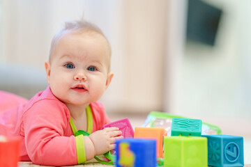 A cute little baby is lying on his stomach and playing cubes