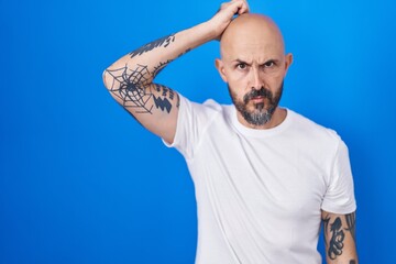 Hispanic man with tattoos standing over blue background confuse and wondering about question....