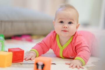 A cute little baby is lying on his stomach and playing cubes