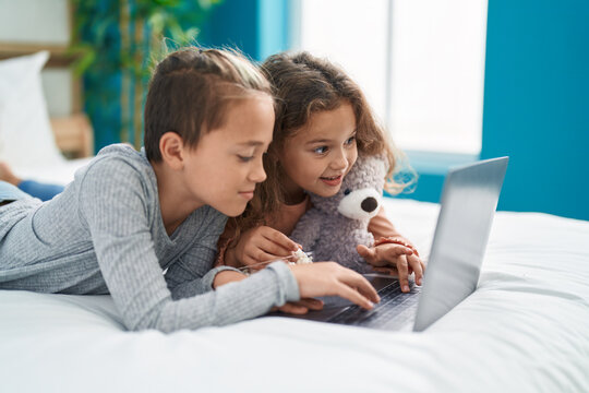 Two kids watching movie on laptop lying on bed at bedroom