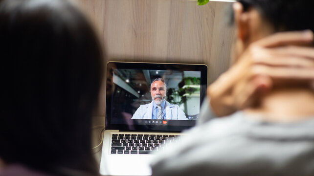 Back view. Asian mother and sick son listening consultation to psychologist doctor on online video call conference consult by laptop computer. Doctor online consultation and telehealth medicine