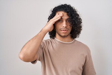 Fototapeta na wymiar Hispanic man with curly hair standing over white background worried and stressed about a problem with hand on forehead, nervous and anxious for crisis