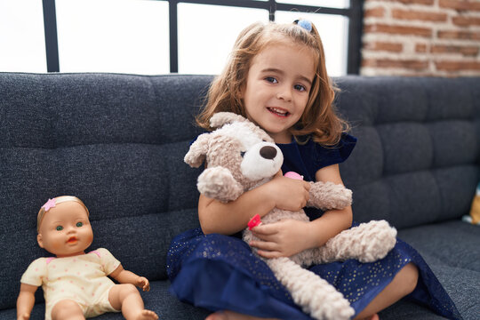Adorable hispanic girl hugging rabbit toy sitting on sofa at home