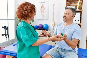 Middle age man and woman wearing physiotherapy uniform having rehab session using balls at physiotherapy clinic