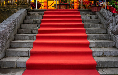 View from below of a rolled out red carpet on a stone staircase. The entrance to a gala or an event.
