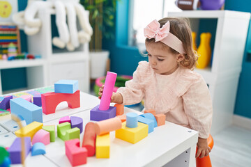 Adorable blonde toddler playing with construction blocks standing at kindergarten