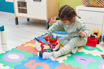 Adorable hispanic toddler playing with supermarket toy sitting on floor at kindergarten