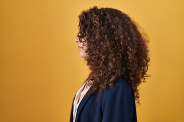 Fototapeta na wymiar Hispanic woman with curly hair standing over yellow background looking to side, relax profile pose with natural face with confident smile.