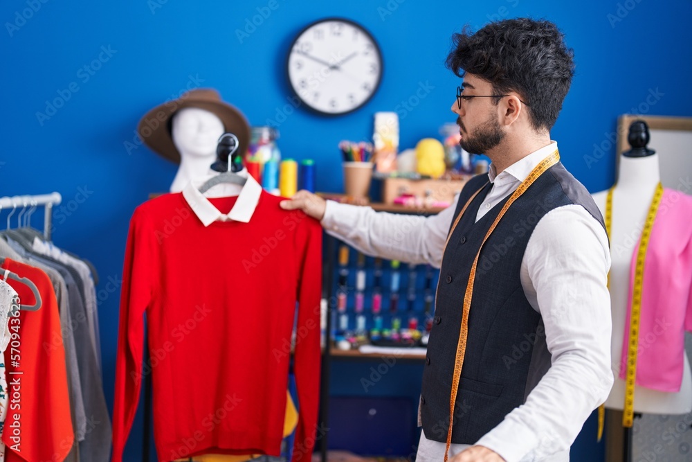 Sticker Young hispanic man tailor holding clothes on rack at sewing studio