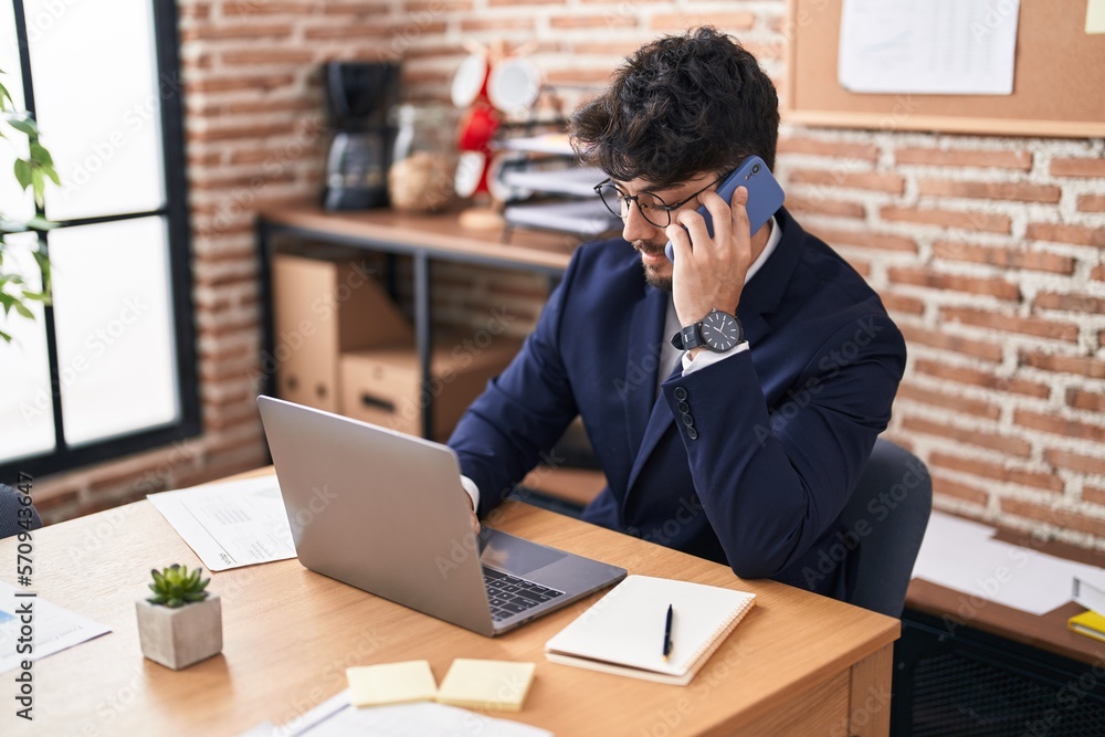 Sticker young hispanic man business worker using laptop talking on smartphone at office