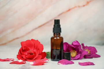 Rose face mist, rose face water, organic natural face serum, flowers extract. Amber glass spray bottle on marble background with red and wild pink rose.  