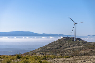 View from the top at the Caramulo mountains to the Serra da Estrela mountains, amazing fog and view over Viseu city, wind turbine or windmill on top, Portugal... - obrazy, fototapety, plakaty