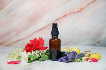 Fototapeta na wymiar Floral face and body mist in amber spray bottle with lavender, rose, lemon, jasmine and elderflowers on marble background. 