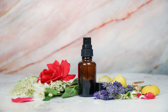 Floral face and body mist in amber spray bottle with lavender, rose, lemon, jasmine and                       elderflowers on marble background. 