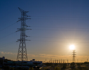 Central eléctrica, torre alta tensión al atardecer con sol en contraluz