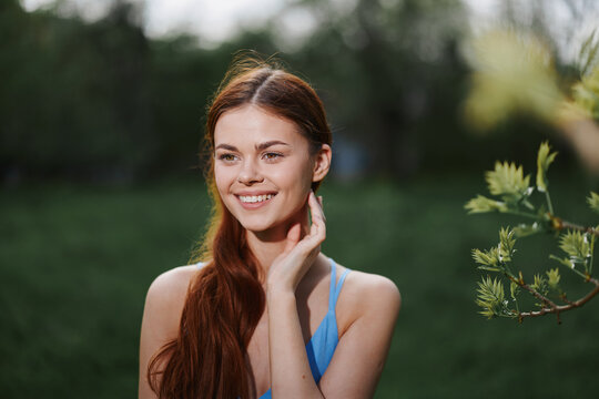 Portrait of a young woman with a beautiful smile with teeth in nature on the background of trees in the spring on a sunny day, the beauty of health and youth, happiness, freedom