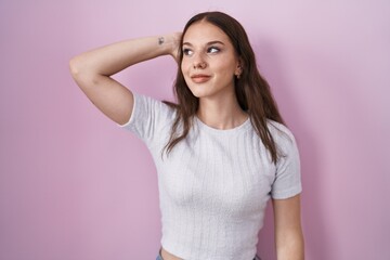 Fototapeta premium Young hispanic girl standing over pink background smiling confident touching hair with hand up gesture, posing attractive and fashionable