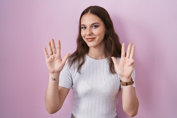 Young hispanic girl standing over pink background showing and pointing up with fingers number nine while smiling confident and happy.