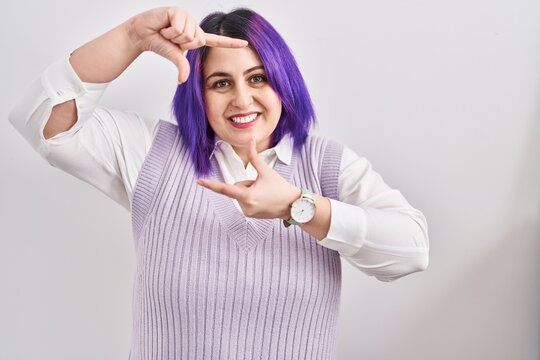 Plus size woman wit purple hair standing over white background smiling making frame with hands and fingers with happy face. creativity and photography concept.