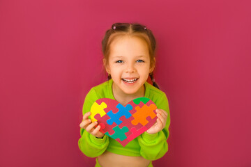 A cheerful happy girl shows a heart from a puzzle - a symbol of support for children with autism...