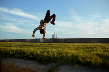 Back view of boy flying in air upside down during his back flip trick pictured on background of...