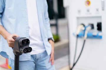 Unrecognizable Asian man holding AC type 2 EV charging connector at EV charging station, man preparing an EV - electric vehicle charging connector for recharge a vehicle.