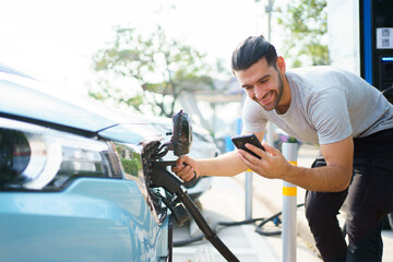 Handsome Asian young man holding an EV plug connector and attaching onto the car.