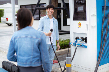 Asian man and woman holding AC type 2 EV charging connector at EV charging station.