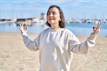Middle age woman smiling confident training yoga at seaside