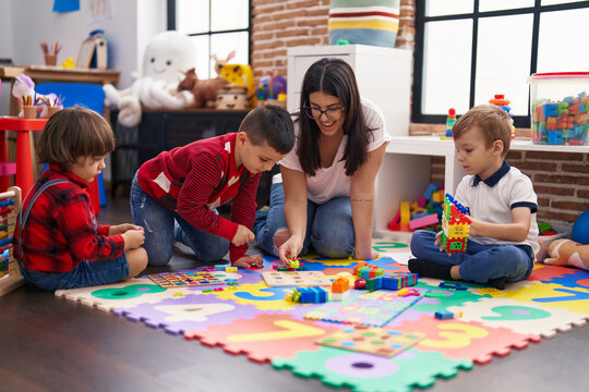 Teacher with group of boys playing with maths puzzle game sitting on floor at kindergarten