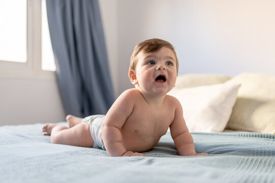 baby less than one year old on all fours on top of bed, 8 month old in diaper on double bed face down, blue-eyed blond-haired baby boy