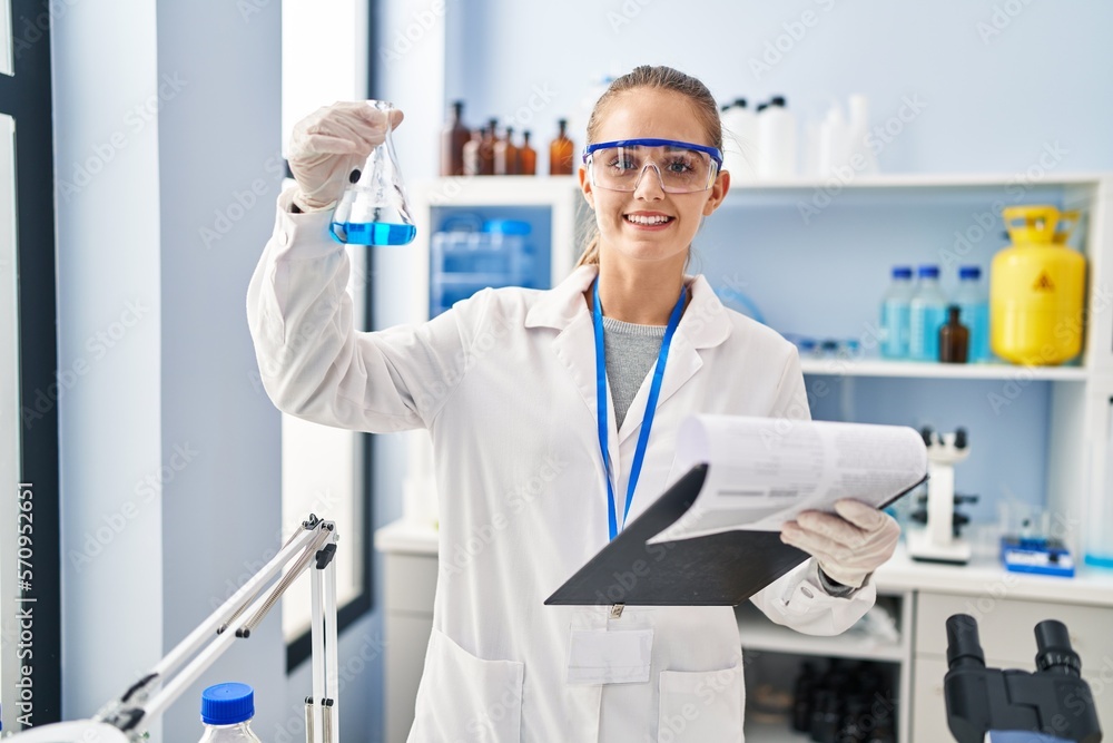 Canvas Prints young blonde woman wearing scientist uniform holding test tube and clipboard at laboratory