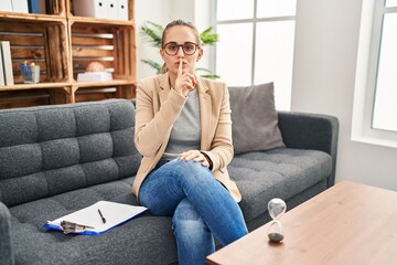 Fototapeta premium Young woman working at consultation office asking to be quiet with finger on lips. silence and secret concept.