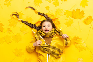 A very surprised little girl on an autumn background with maple leaves and in a waterproof raincoat from the rain.