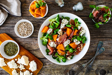 Tasty salad - prosciutto crudo, sweet potatoes, smoked white cheese and fresh vegetables on wooden...