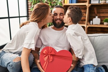 Obraz premium Family kissing father holding heart box gift at home