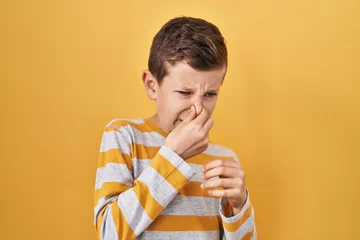 Foto op Canvas Young caucasian kid standing over yellow background smelling something stinky and disgusting, intolerable smell, holding breath with fingers on nose. bad smell © Krakenimages.com