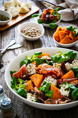Tasty salad - prosciutto crudo, sweet potatoes, smoked white cheese and fresh vegetables on wooden table
