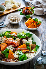 Tasty salad - prosciutto crudo, sweet potatoes, smoked white cheese and fresh vegetables on wooden table
