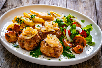Fried pork meatballs with fried onion, french fries and fresh vegetables on wooden table
