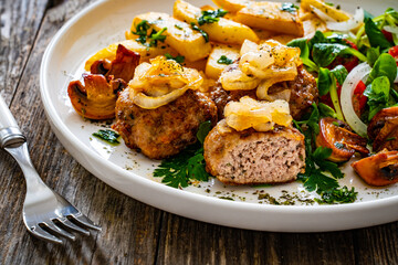 Fried pork meatballs with fried onion, french fries and fresh vegetables on wooden table
