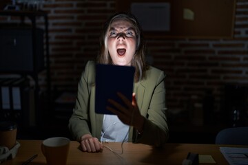 Blonde caucasian woman working at the office at night angry and mad screaming frustrated and furious, shouting with anger. rage and aggressive concept.